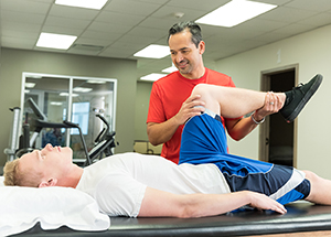 Man lying on back on table. Healthcare provider is raising one of his legs.